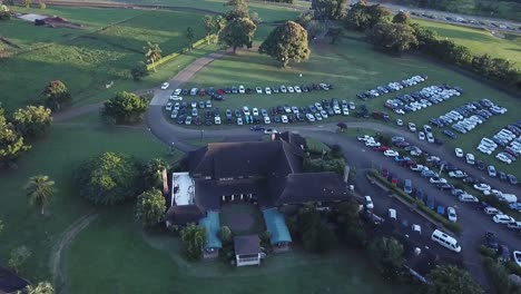 View-Of-Rooftop-And-Parking-Lot-With-Cars-On-Green-Landscape-In-Kauai,-Hawaii-On-A-Sunset---drone-pullback