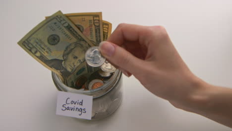 A-caucasian-woman's-hand-puts-two-American-quarters-into-a-"Covid-Savings"-jar
