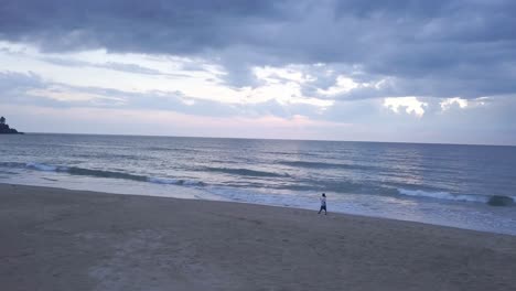 Cloudscape-Over-Splashing-Sea-Waves-With-Tourist-Walking-On-Sandy-Seashore-During-Sunset-At-Rajbaga-Beach-In-Canacona,-South-Goa,-India