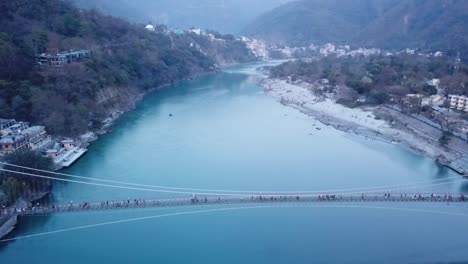 Pedestrians-Crossing-Ganges-River-Through-Ram-Jhula-In-Rishikesh,-India---aerial-drone