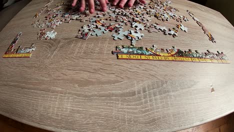 Hands-assembling-jigsaw-puzzle-of-ancient-world-map-on-wooden-table,-time-lapse