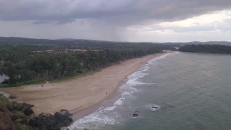 Aerial-View-Of-Sandy-Beach-And-Ocean-Coast-On-A-Cloudy-Day-At-Rajbagh-Beach,-Canacona,-South-Goa,-India---aerial-pullback
