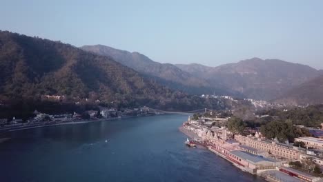 Vista-Panorámica-Del-Río-Sagrado-Ganges-Que-Fluye-A-Través-De-Las-Verdes-Montañas-De-Rishikesh,-Uttarakhand,-India---Toma-Aérea-De-Drones