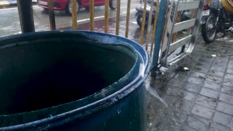 Rainwater-From-The-Roof-Falling-And-Splashing-At-The-Edge-Of-An-Empty-Blue-Barrel---Closeup-Shot