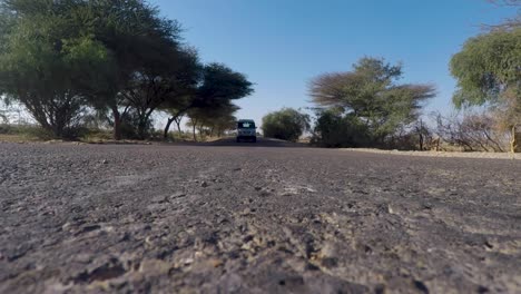 Vista-A-Nivel-Del-Suelo-De-Un-Vehículo-Que-Se-Acerca-Y-Pasa-Por-Encima-De-La-Cámara-En-La-Carretera-Apshalt-En-Rajasthan:-Plano-Lejano