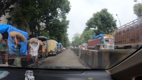 Driving-Car-On-The-Narrow-Street-Between-Concrete-Barriers-And-Parked-Vehicles-In-Mumbai,-India---POV-shot