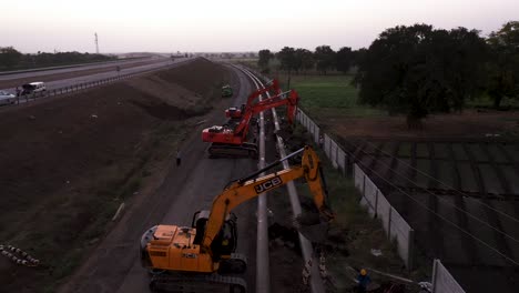 Camiones-Excavadoras-Y-Personas-Realizando-Trabajos-De-Tubería-Y-Construcción-Cerca-De-La-Carretera.