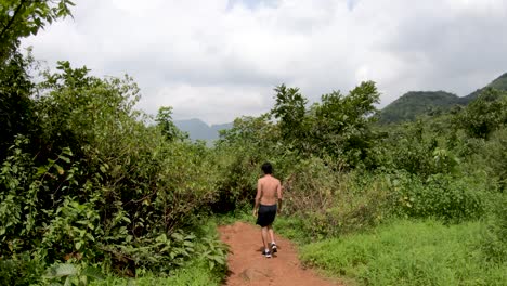 View-Behind-A-Shirtless-Man-Walking-On-The-Pathway-In-The-Tropical-Forest-On-The-Hill-In-Maharashtra,-India---wide-slowmo-shot