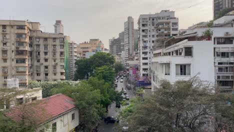 Straße-Zwischen-Alten-Gebäuden-Mit-Vorbeifahrenden-Autos-Und-Motorrädern-In-Der-Stadt-Mumbai,-Indien