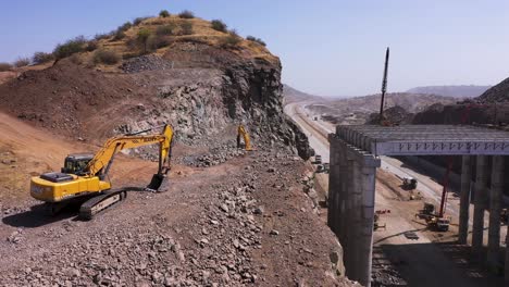 Immobile-Excavator-Trucks-On-Top-Of-A-Mountain-Cliff-For-Pipeline-Construction,-Beside-The-Public-Highway-During-The-Day