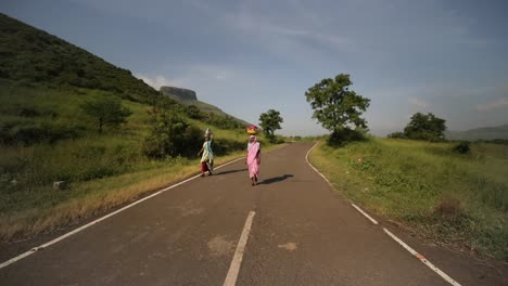 Indian-Locals-Carrying-Basket-And-Container-On-Their-Heads,-Walk-On-Empty-Road-In-Trimbakeshwar