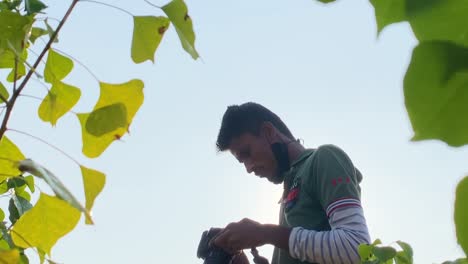 Zooming-out-clip-of-south-asian-photographer-taking-a-photo,-with-leaves-around-him-blowing-in-gentle-breeze