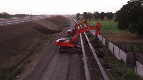Forward-Aerial-View-Of-Three-Excavator-Trucks-Near-A-Highway,-During-The-Day