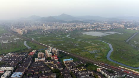 Panoramic-View-of-Cityscape-with-Suburban-Railway-Lines-in-Vasai,-India---aerial-drone-shot