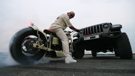 Low-angle-shot-of-a-motorcyclist-doing-a-burnout-on-a-bike-in-front-of-an-SUV