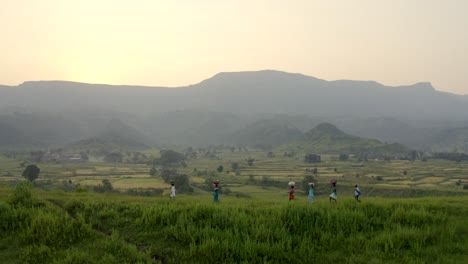 People-Carrying-Bag-On-Their-Head-While-Walking-In-The-Green-Hills-At-Sunrise