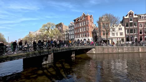 Turistas-Haciendo-Cola-Sobre-El-Puente-Del-Canal-Para-Visitar-Un-Lugar-Turístico-En-Amsterdam