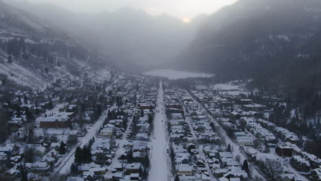 Aerial-drone-view-of-Telluride-mountain-ski-resort-downtown-Colorado-fresh-snow-and-fog-of-scenic-mountains-landscape-and-historic-buildings-trucks-and-cars-morning-winter-backward-pan-movement