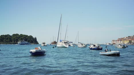 Barcos-De-Diferentes-Tamaños-Flotando-Pacíficamente-En-Un-Pequeño-Puerto-Junto-A-La-Costa