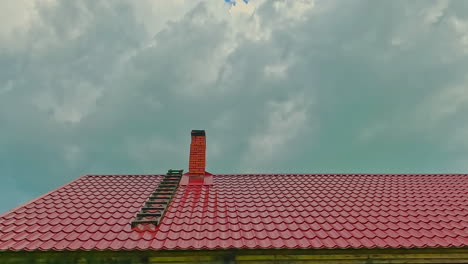 Wolken-Ziehen-über-Rotes-Dach-Mit-Schornstein-Und-Leiter