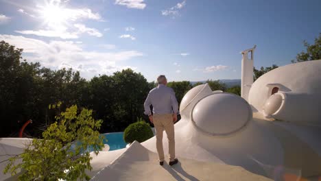 Middle-Aged-Man-Walking-on-the-Rooftop-of-a-Bubble-House-with-Large-Windows-on-a-Sunny-Day
