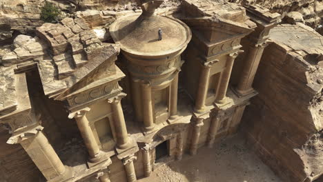 Arab-on-top-of-the-famous-El-Deir-Monastery,-in-sunny-Jordan---Aerial-tilt-reveal