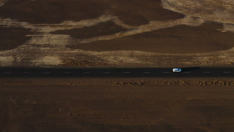 Car-driving-on-a-road,-close-to-desert-dunes,-sunset-in-Namibia---Aerial-tilt-reveal