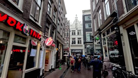 Eine-POV-Aufnahme-Beim-Spaziergang-Durch-Die-Enge,-überfüllte-Warmoesstraat,-Umgeben-Von-Restaurants-Und-Einzelhandelsgeschäften,-An-Einem-Kalten,-Regnerischen-Tag-In-Amsterdam,-Niederlande