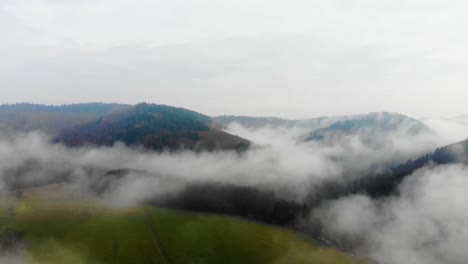 Drone-view-flying-over-the-green-field-in-the-Baden-Württemberg,-Odenwald-Nature-park-on-a-foggy-day,-Germany