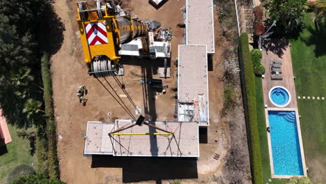 Aerial-view-looking-down-over-large-crane-lifting-modern-modular-home-installing-onto-building-site-foundation