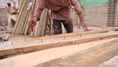 Carpenter-Hammering-Out-Nails-From-Planks-Of-Wood-On-Construction-Site
