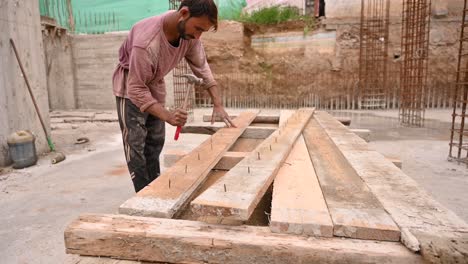 Male-Labourer-Hammering-Out-Nails-From-Planks-Of-Wood-On-Construction-Site