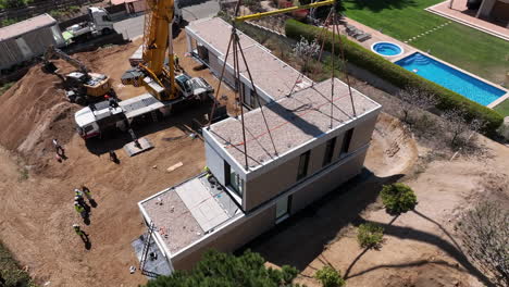 Modular-housing-suspended-by-crane-installed-onto-foundation-plot,-Aerial-orbiting-view