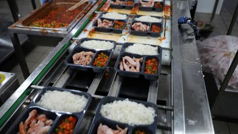 Prepared-meals-in-plastic-packages-on-conveyor-belt-in-professional-kitchen