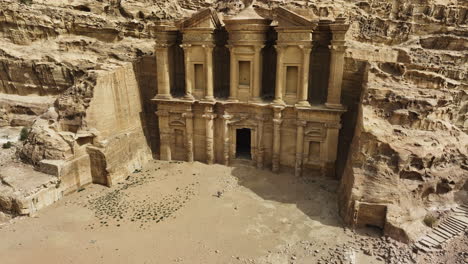 Aerial-view-around-a-person-walking-in-front-of-the-El-Deir-Monastery,-in-sunny-Jordan