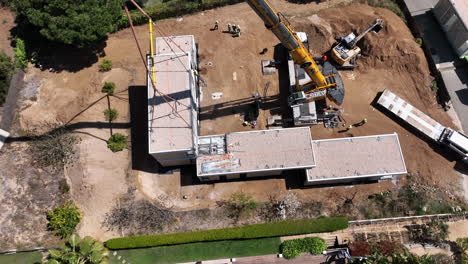 Aerial-view-circling-sustainable-modular-housing-construction-site-with-heavy-crane-lift-machinery