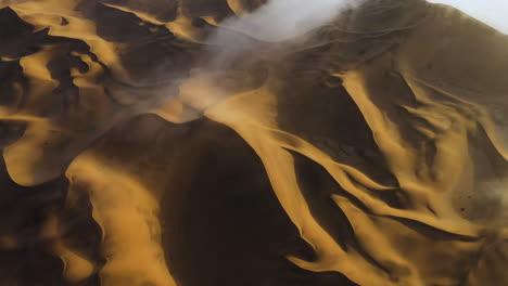 Desert-landscape-with-shapes-of-sand-and-fog,-during-sunrise---Aerial-tilt-reveal