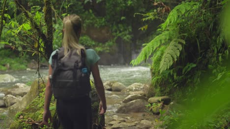Sportive-blond-female-tourist-with-backpack-walking-in-tropical-river-valley