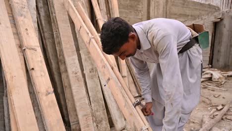 Pakistani-Labourer-Using-Hammer-To-Split-Wooden-Planks-On-Construction-Site