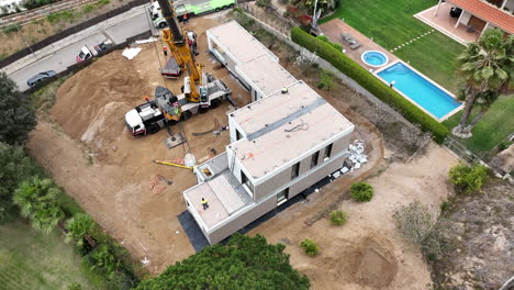 Aerial-view-above-large-crane-lifting-smart-modular-home-structure-onto-building-site-foundation