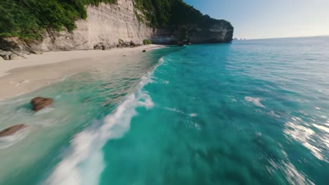 Spectaculair-FPV-drone-aerial-of-a-cliff-spinning-into-tropical-bright-waters,-circling-a-rock-on-sunny-beach-dream-destination