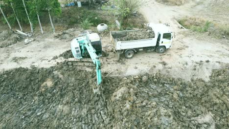 Aerial-drone-view-of-backhoe-machinery-digging-the-soil-to-load-a-dump-truck