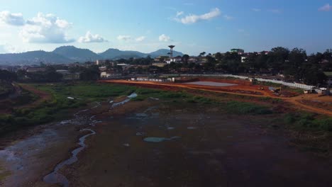 Aerial-view-low-over-the-dry-Lac-Municipal-lake,-drought-in-sunny-Yaounde,-Cameroon---reverse,-drone-shot