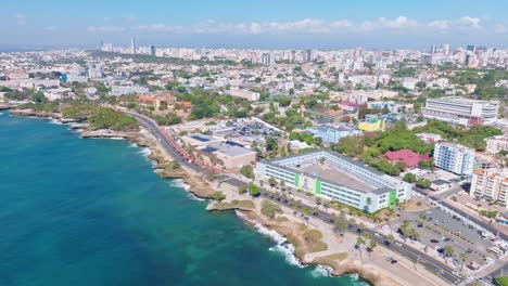 Aerial-flyover-coastline-of-Santo-Domingo-cityscape-and-traffic-on-coastal-road-during-sunny-day---Dominican-Republic