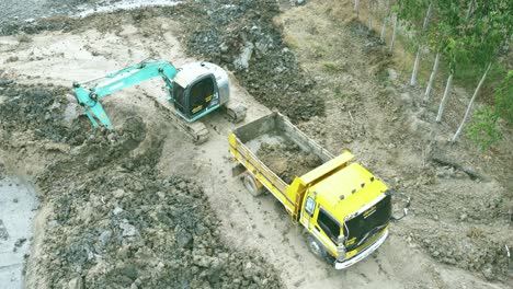 Aerial-drone-view-of-backhoe-machinery-digging-the-soil-to-load-a-dump-truck