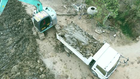 Aerial-drone-view-of-backhoe-machinery-digging-the-soil-to-load-a-dump-truck