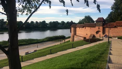 Nogat-river-waterfront-in-Malbork,-Poland-at-beautiful-sunset-with-a-castle,-the-red-brick-walls-and-unrecognizable-people