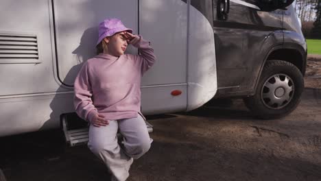 Portrait-of-a-girl-in-a-pink-hat-sitting-on-the-steps-of-a-caravan,-exposing-her-face-to-the-sun