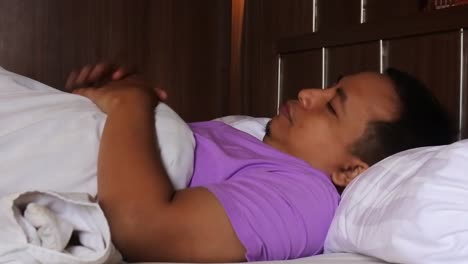 An-asian-man-getting-ready-for-bed-but-with-a-restless-expression-in-his-bed,-HD-video