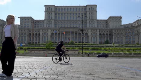 Elegante-Frau-In-Einem-Weißen-T-Shirt,-Die-Auf-Die-Kamera-Zugeht-Und-Die-Aussicht-Genießt,-Im-Hintergrund-Der-Parlamentspalast,-Bukarest,-Rumänien